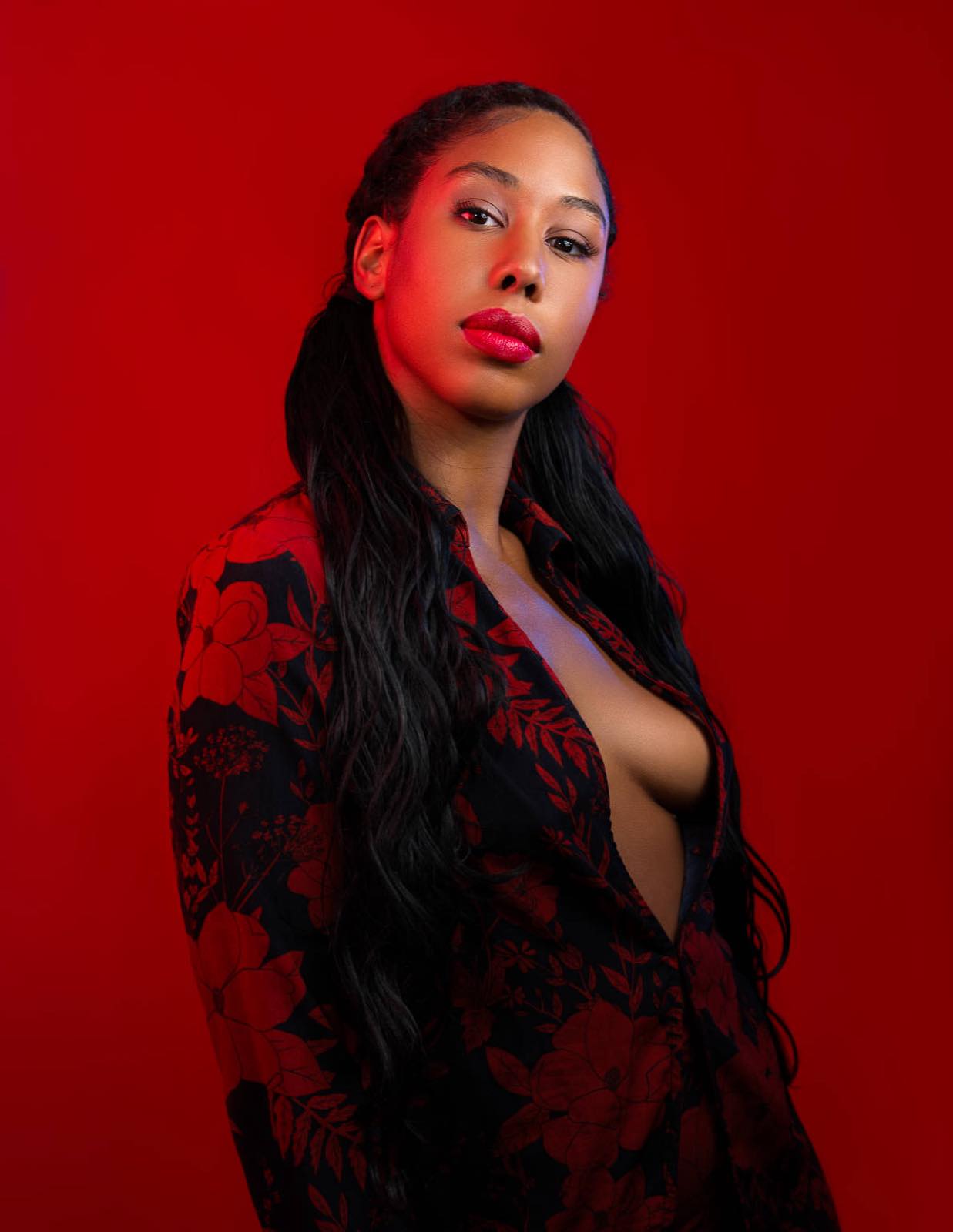 Portrait en studio sur fond rouge, robe fleurie et regard direct